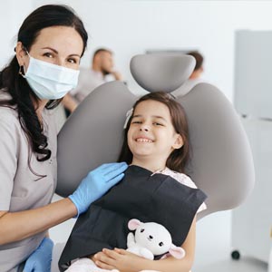 A young girl in a dentist's chair holding a stuffed animal